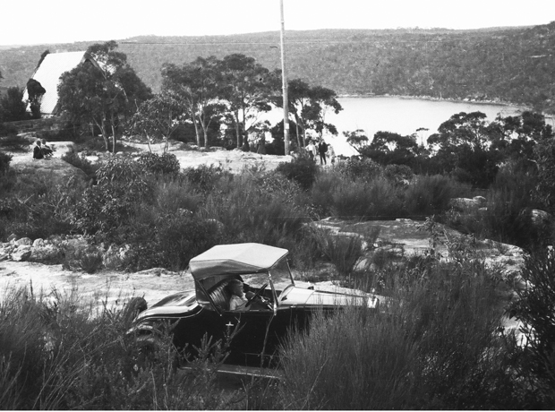 Man sitting in motor car with Pinnacle house in bushland